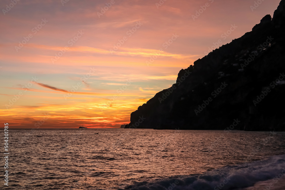 Panoramic sunset view from Marina Grande beach in Positano at Amalfi Coast, Italy, Campania, Europe. Silhouette of coastline. Orange twilight over Li Galli islands in Mediterranean Sea. Reflection