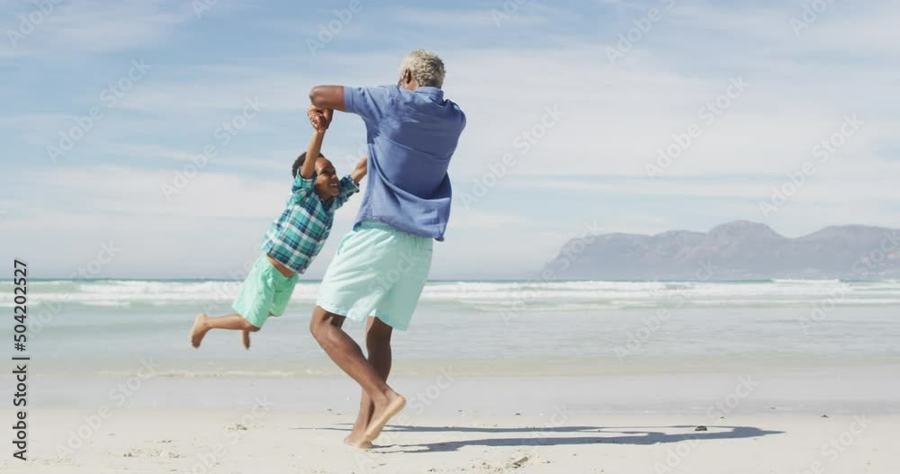Happy senior african american father playing with son on sunny beach