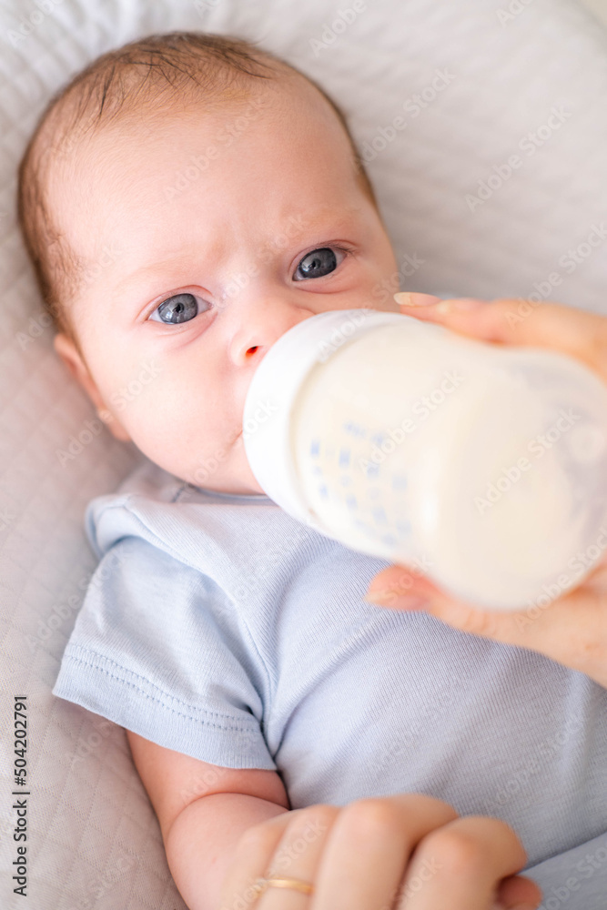 loving mother feeding her little boy child with milk baby bottle at home, portrait infant Baby eating, drinking powdered milk, looking at camera loving mother feeding her little boy child with milk baby bottle at home, portrait infant Baby eating, drinking powdered milk, looking at camera