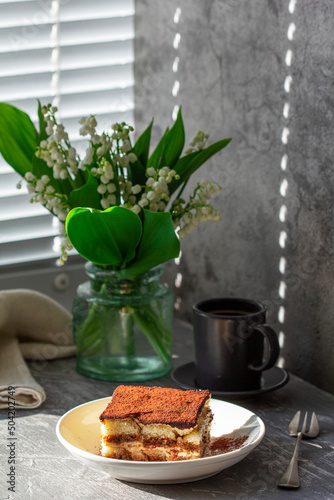 Obraz na płótnie Traditional Italian dessert tiramisu, coffee and a bouquet of lilies of the valley on a gray concrete background. w salonie