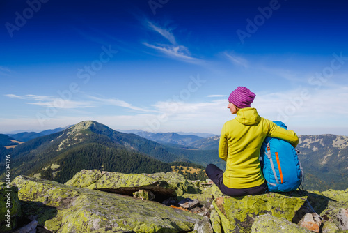 Rear view of Woman Traveler with Backpack sitting on the rock and enjoying the Mountain view on sunny day