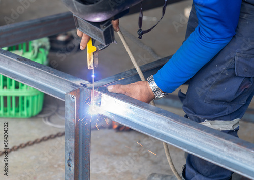 Worker welding leg of table with his hands, sparks without gloves.