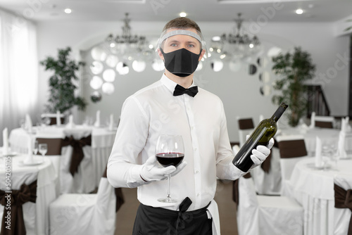 Waiter in a protective mask with a glass of red wine in his hands.