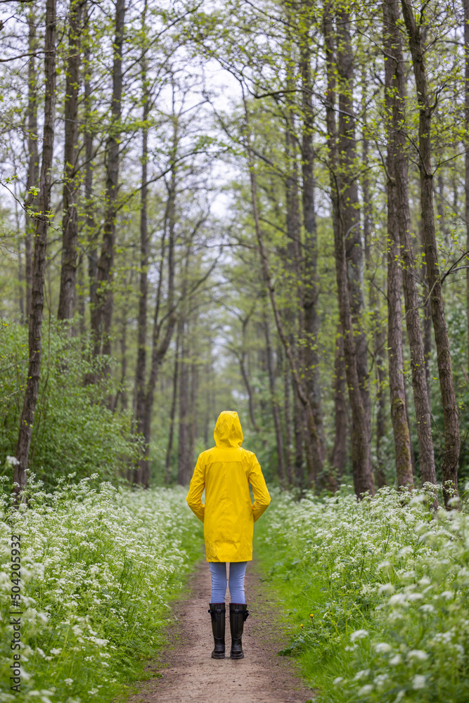 Obraz premium Young woman with yellow raincoat and rubber boots in spring nature