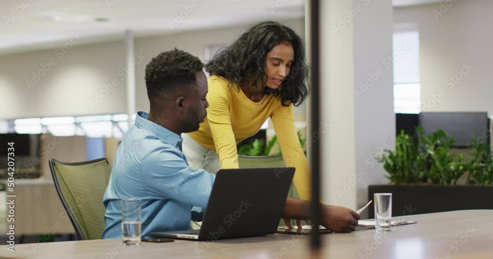 Video of happy diverse businessman and businesswoman using laptop, talking about project Video of happy diverse businessman and businesswoman using laptop, talking about project