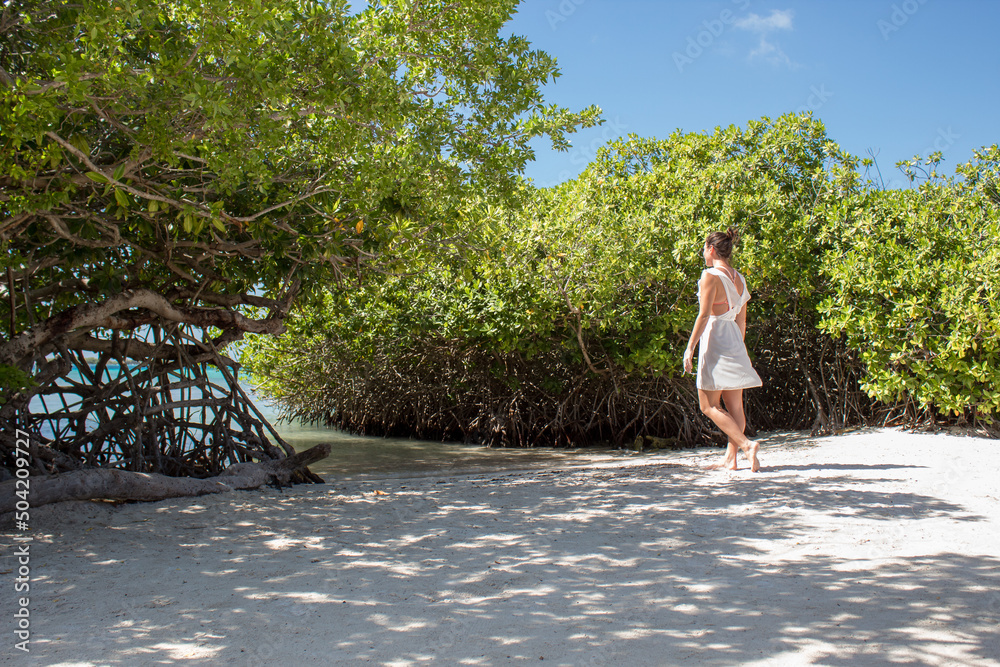 Fototapeta premium woman in white dress walking towards water on beach