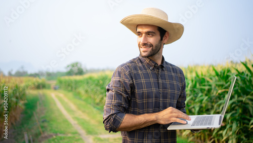 Handsome male farmer Middle Eastern American smiling holding 
 laptop,tablet in corn fields,barley and wheat to use a fertilization log program.Plant growth, production and contact online customer.