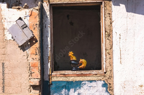 Ukrainian ceramic rooster, ceramic rooster stands in the reflected window of the ruined house photo