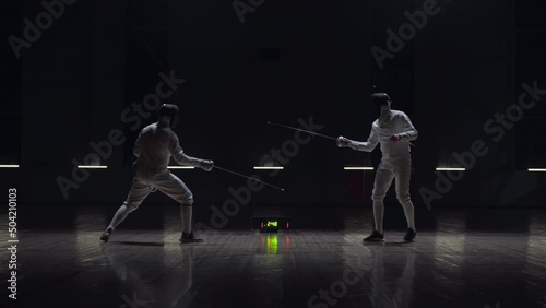 Two professional male fencers having a sabre fight in against dark background