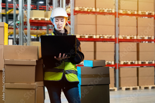Customs clearance of goods. Woman with laptop in warehouse. Warehouse of customs company. Woman is engaged in customs clearance. Girl stands with laptop among boxes. Girl in work uniform in warehouse