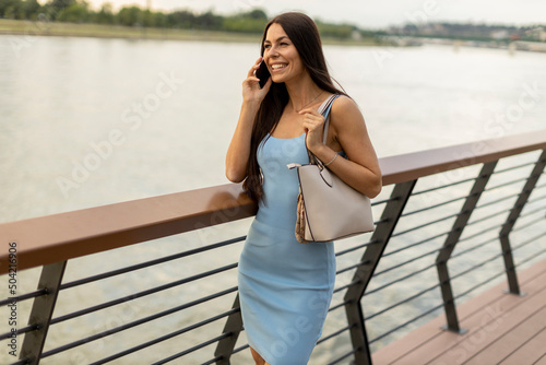 Young woman using a mobile phone while walking on the river promenade © BGStock72