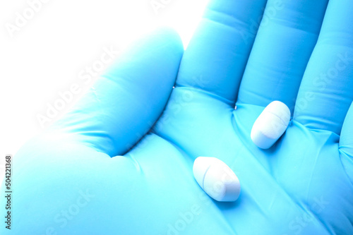 a hand in a blue medical glove holds a white pill. close-up