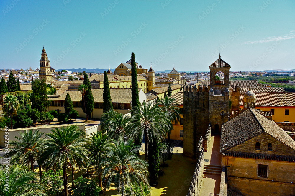 View from the height of the cityscape of Cordoba, Spain, with the mosque in the background and a palm tree garden in the foreground surrounded by a stone wall
