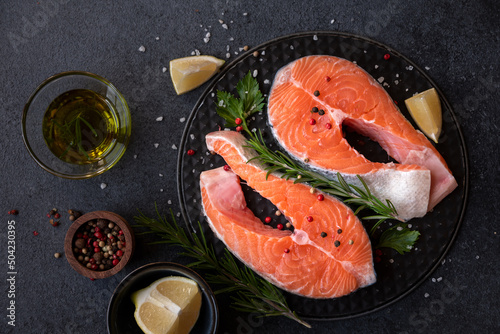 Uncooked raw salmon fish with herbs on dark background