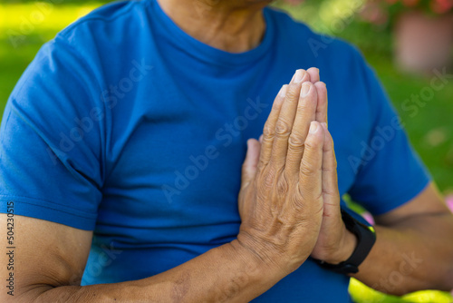 Midsection of biracial senior man meditating in prayer position while sitting in yard