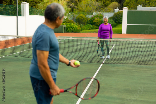 Smiling biracial senior woman playing tennis with senior husband at tennis court © wavebreak3
