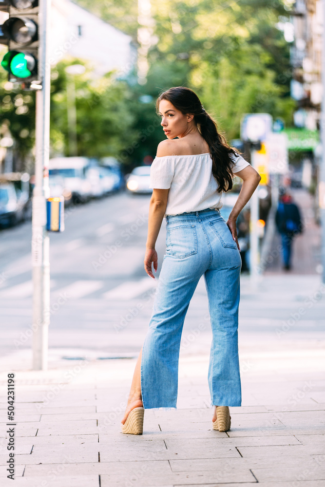 Full length portrait of beautiful female posing on street. Caucasian model dressed in casual jeans and shirt during fashion photo session