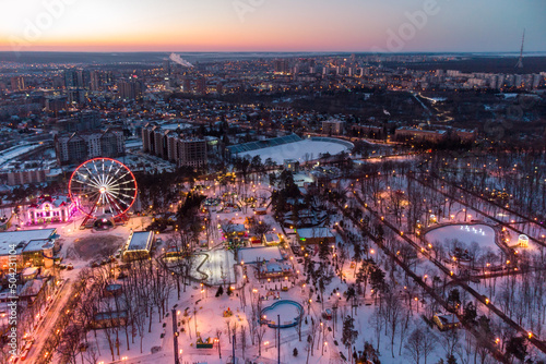 Aerial vibrant evening cityscape, Ferris wheel and entertainments in winter, covered in white snow. Kharkiv city center in sunset colors, amusement Gorky Central Park