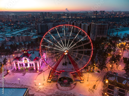 Aerial illuminated Ferris wheel. Winter Kharkiv city center recreation area in evening lights. Amusement Gorky Central Park in sunset