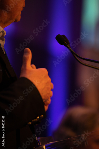 gros plan sur les mains d'un homme faisant un discours devant un pupitre avec des micros. il fait des gestes avec ses mains 