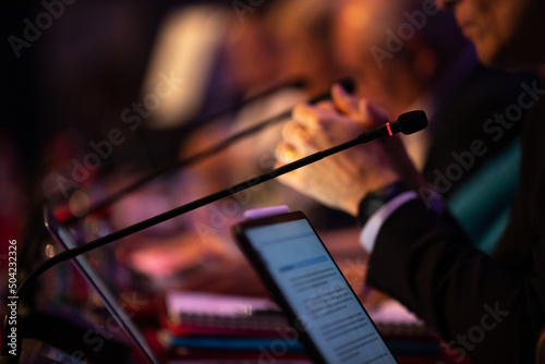 focus sur un micro et les mains d'un orateur prononçant un discours à la tribune lors d'un meeting politique, d'un colloque ou d'une réunion