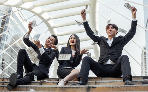 Three smart happy Asian businesspeople wearing formal suits, dreaming, smiling with happiness, success and confidence, having a lot of money, banknotes in the air. Business Concept.