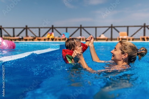 Fototapeta Naklejka Na Ścianę i Meble -  Mom plays with her son with oversleeves in the pool in summer