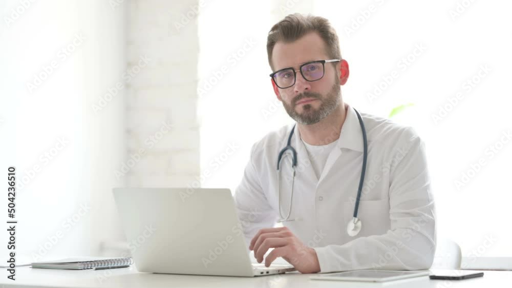 Doctor Looking at Camera while using Laptop in Office Doctor Looking at Camera while using Laptop in Office