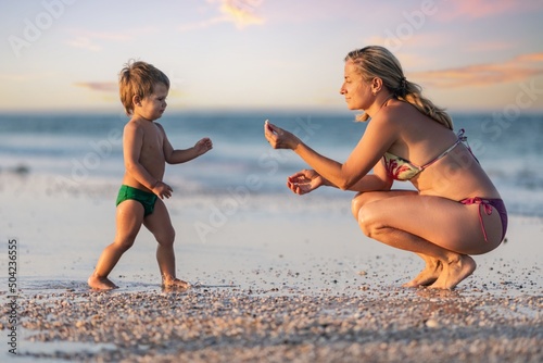 The kid collects shells and pebbles in the sea on a sandy bottom with his mother under the summer sun on vacation