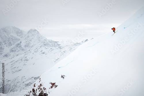 a young man quickly skis down a snow-covered glacier against the backdrop of high mountains