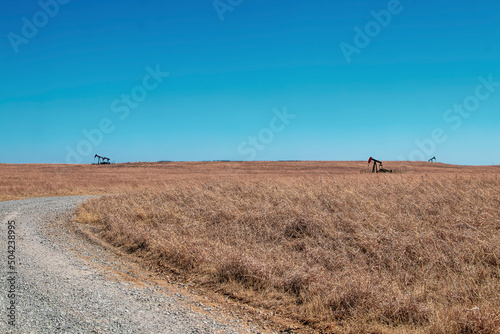 Three distant oil or gas well pumps on prairie grassland with curving gravel road running through it