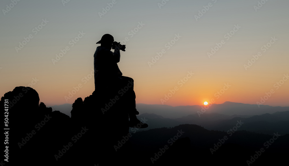 Nature photographer traveler taking photo of beautiful sunset background from a mountain peak.Concept of Adventure travel, mountaineering and photography