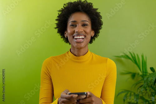Portrait of cheerful afro young african american businesswoman holding smartphone against green wall