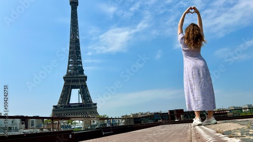 a beautiful girl in a long blue dress stands against the blue sky and the Eiffel Tower in a restaurant. She looks into the frame there is a place for advertising travel agency. High quality photo