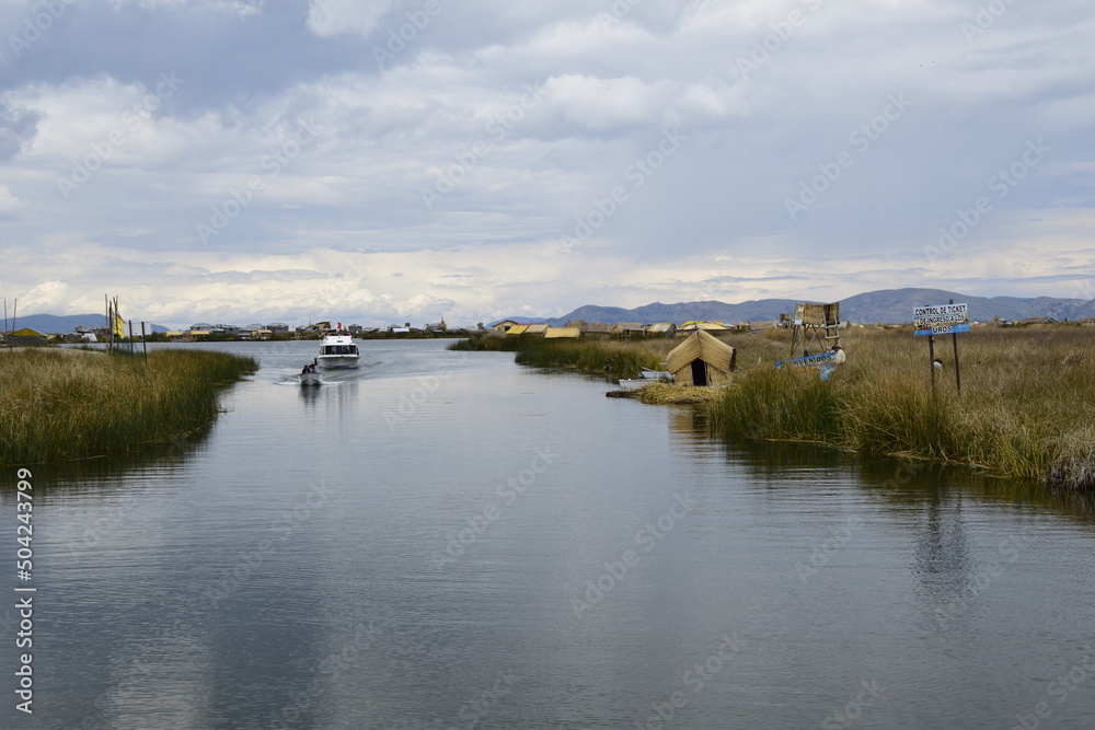 A boat with locals rides along a small waterway on Lake Titicaca to the straw Islands. Puno, Peru.