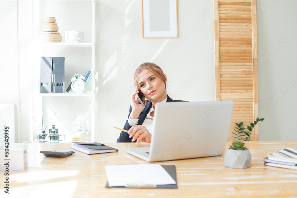 Happy businesswoman talking on the mobile phone and smiling while sitting at her working place in office Happy businesswoman talking on the mobile phone and smiling while sitting at her working place in office