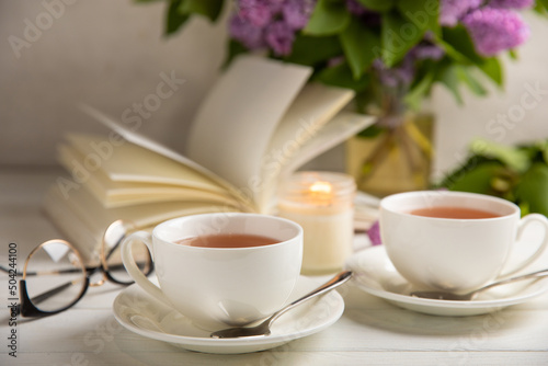 A cup of green tea against the background of a spring bouquet of lilacs on a textured gray background.Romantic composition with books and candles. Spring tea drink. Side view. Place to copy.