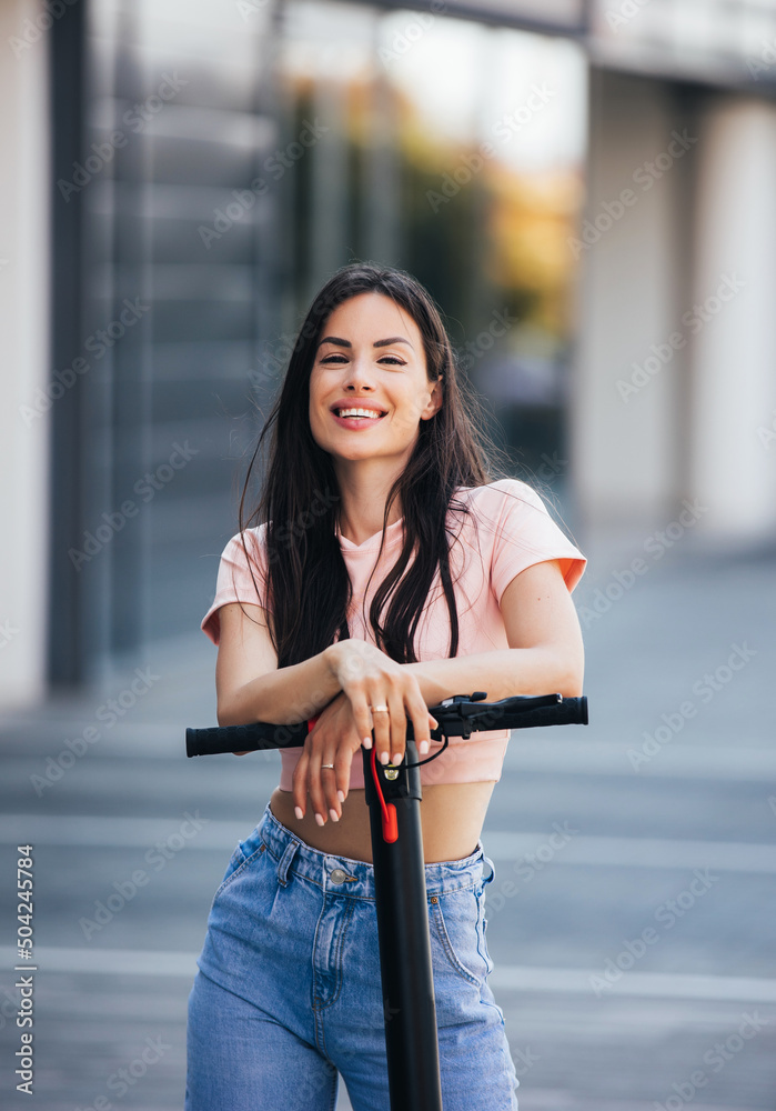 Close up of young woman holding steering column handle grip of electric kick scooter on the street in summer day