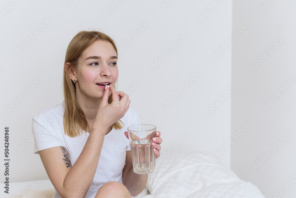 Young beautiful woman take a pill or tablet with a glass of water on bed. Taking sleeping pills and painkillers at home Young beautiful woman take a pill or tablet with a glass of water on bed. Taking sleeping pills and painkillers at home
