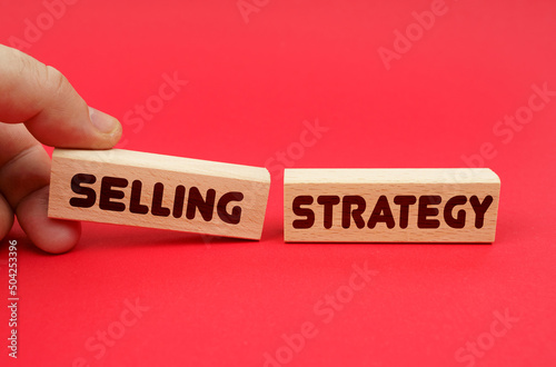 On a red background, wooden blocks, one of them in hand. The blocks are written - SELLING STRATEGY