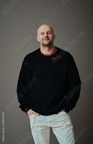 Vertical medium long shot of confident handsome mature Caucasian man standing against gray wall background looking at camera, upcycling fashion concept