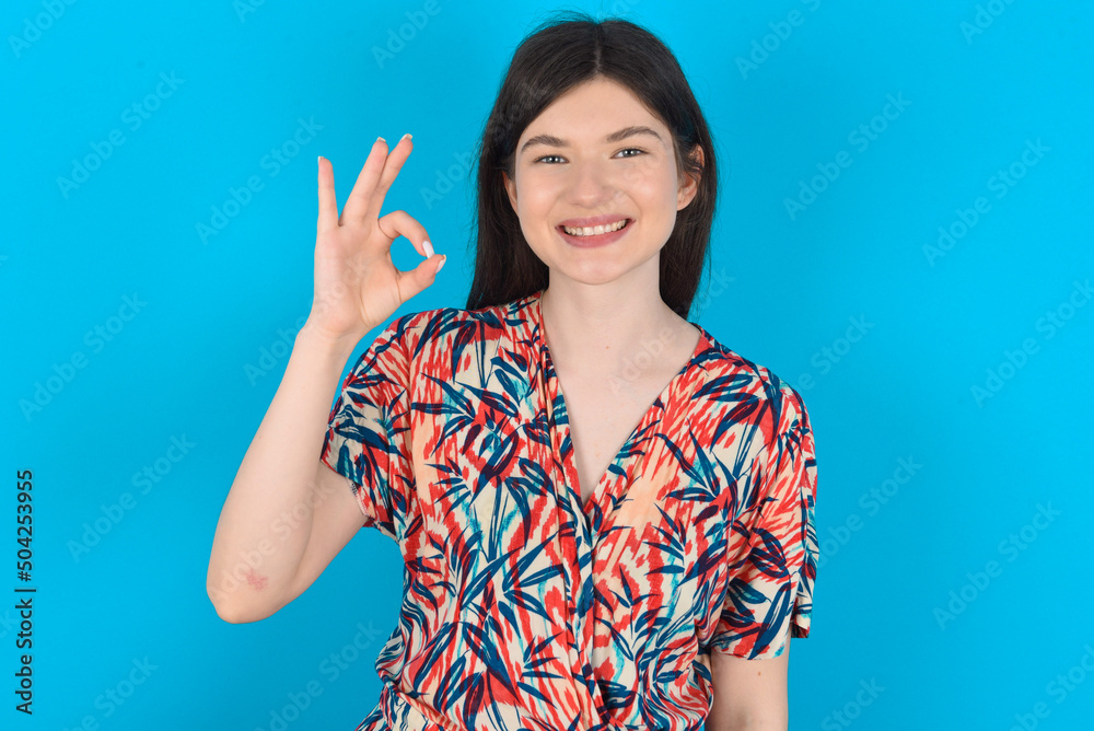young caucasian woman wearing floral dress over blue background hold hand arm okey symbol toothy approve advising novelty news young caucasian woman wearing floral dress over blue background hold hand arm okey symbol toothy approve advising novelty news