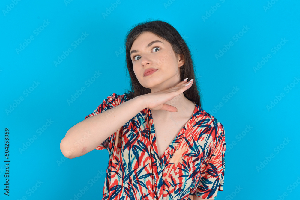 young caucasian woman wearing floral dress over blue background cutting throat with hand as knife, threaten aggression with furious violence.