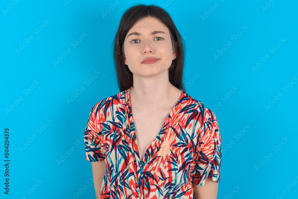 Displeased young caucasian woman wearing floral dress over blue background frowns face feels unhappy has some problems. Negative emotions and feelings concept Displeased young caucasian woman wearing floral dress over blue background frowns face feels unhappy has some problems. Negative emotions and feelings concept