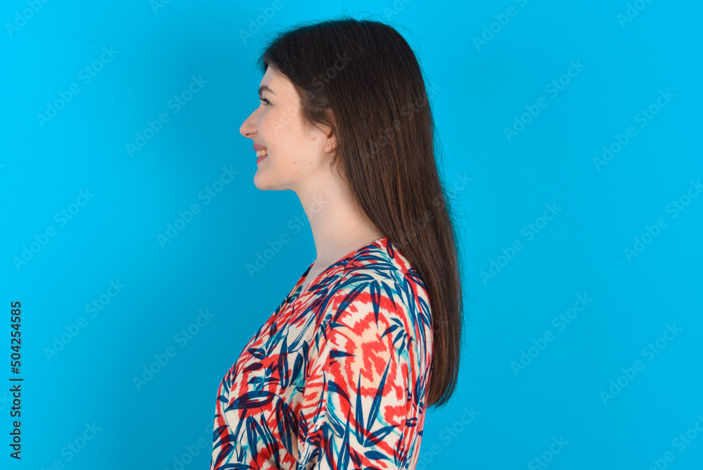 Profile portrait of nice young caucasian woman wearing floral dress over blue background look empty space toothy smile Profile portrait of nice young caucasian woman wearing floral dress over blue background look empty space toothy smile