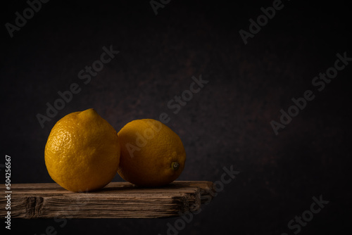 two ripe lemons lie side by side on old boards against a dark backdrop. moody artistic still life with copy space