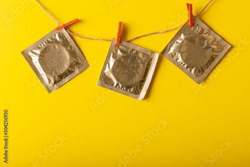 Close-up of condom packages hanging on clothesline with clothespins against yellow background
