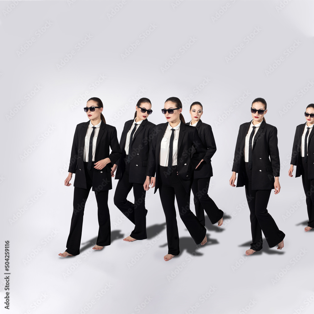 Group of same women in black classic suits, black tie, white shirt and sunglasses walking on white background with copy space and casting black shadow. Model with bare feet and ponytail hairstyle Group of same women in black classic suits, black tie, white shirt and sunglasses walking on white background with copy space and casting black shadow. Model with bare feet and ponytail hairstyle