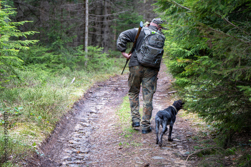 Old Hunter in the woods with his dog. Male hunter hunting with his hunting dog outdoors. German wirehaired pointer. Hunter with his shotgun in middle of nature.