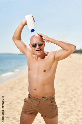 Handsome sexy man relaxing near sea applying sunscreen cream on the head. Funny Summer vacation sea sun tan concept
